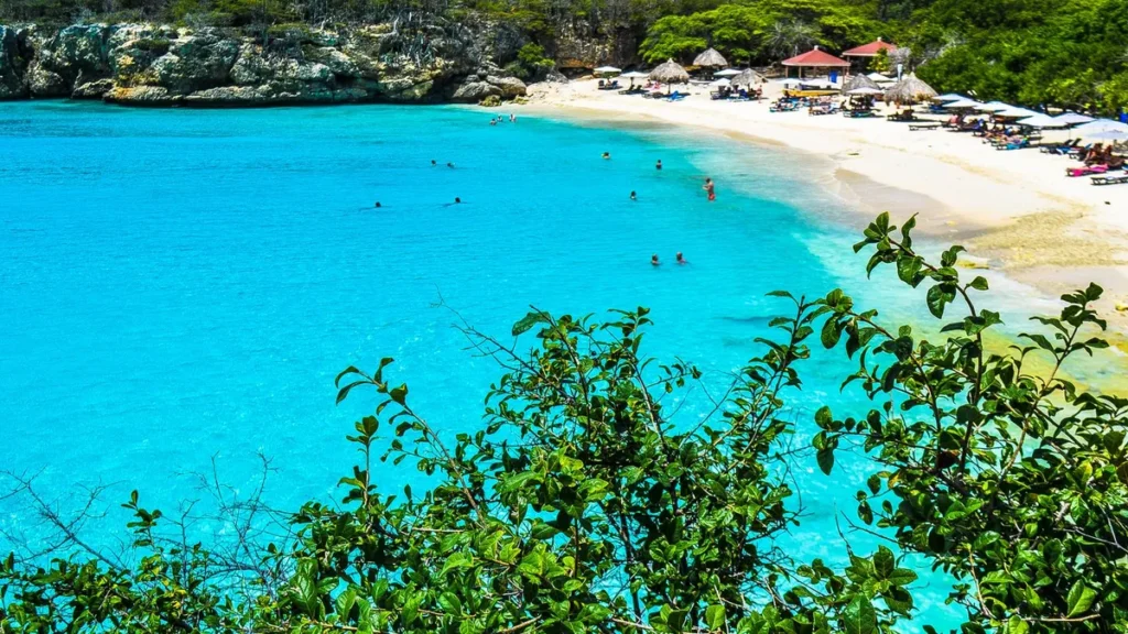 Turquoise baai van Grote Knip op Curaçao met wit zandstrand, parasols en groene heuvels