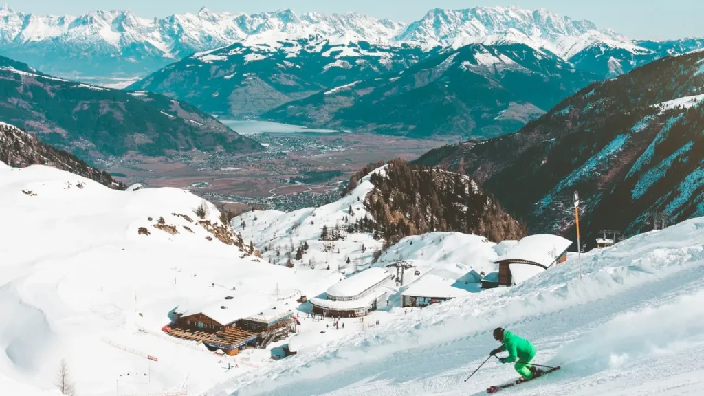 Skiër in groen pak op een zonnige piste bij Kaprun met besneeuwde bergen en het meer van Zell am See