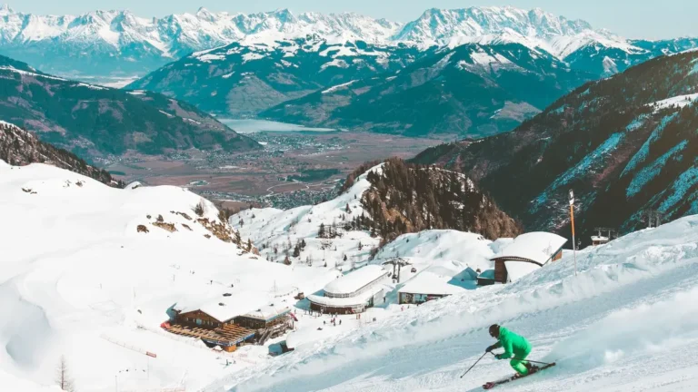 Skiër in groen pak op een zonnige piste bij Kaprun met besneeuwde bergen en het meer van Zell am See