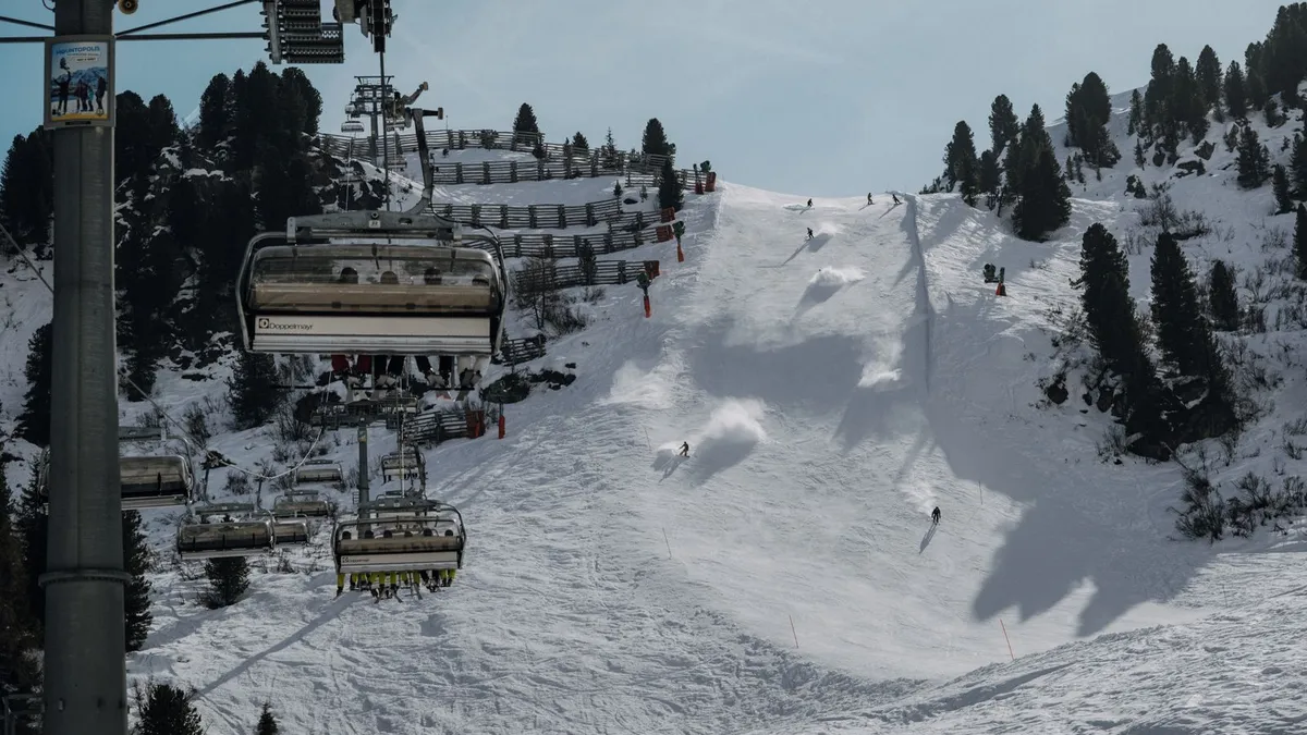 Stoeltjeslift boven een besneeuwde piste met skiërs en dennenbomen in Tirol