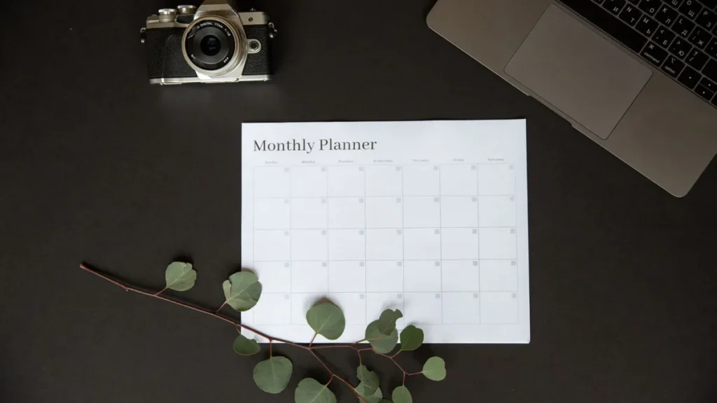 Maandplanner naast een laptop en camera voor het plannen van een lastminute wintervakantie