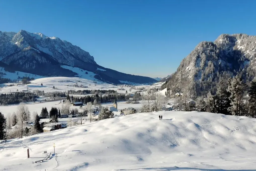 Besneeuwd dorp aan de Walchsee in Tirol met bergen en blauwe lucht